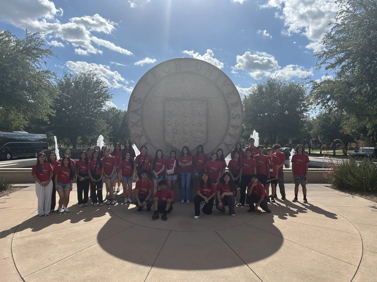 A Landmark student group in matching trip shirts at the Texas Tech University seal, with their motorcoach parked behind them