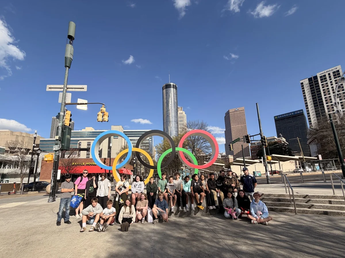 A Landmark student group seated at the Olympic Rings sculpture with the downtown Atlanta skyline behind them