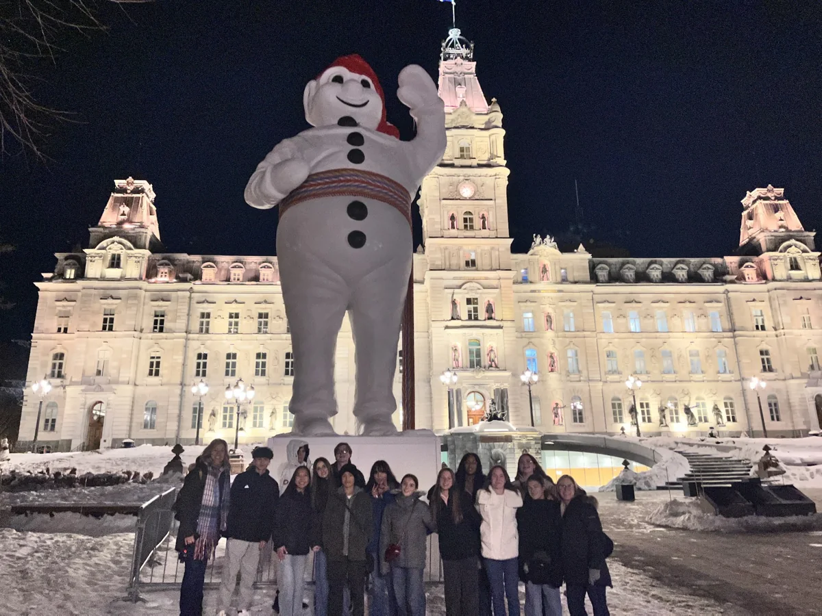 A Landmark student group at night beside the Bonhomme statue in front of the Quebec Parliament Building during Winter Carnival