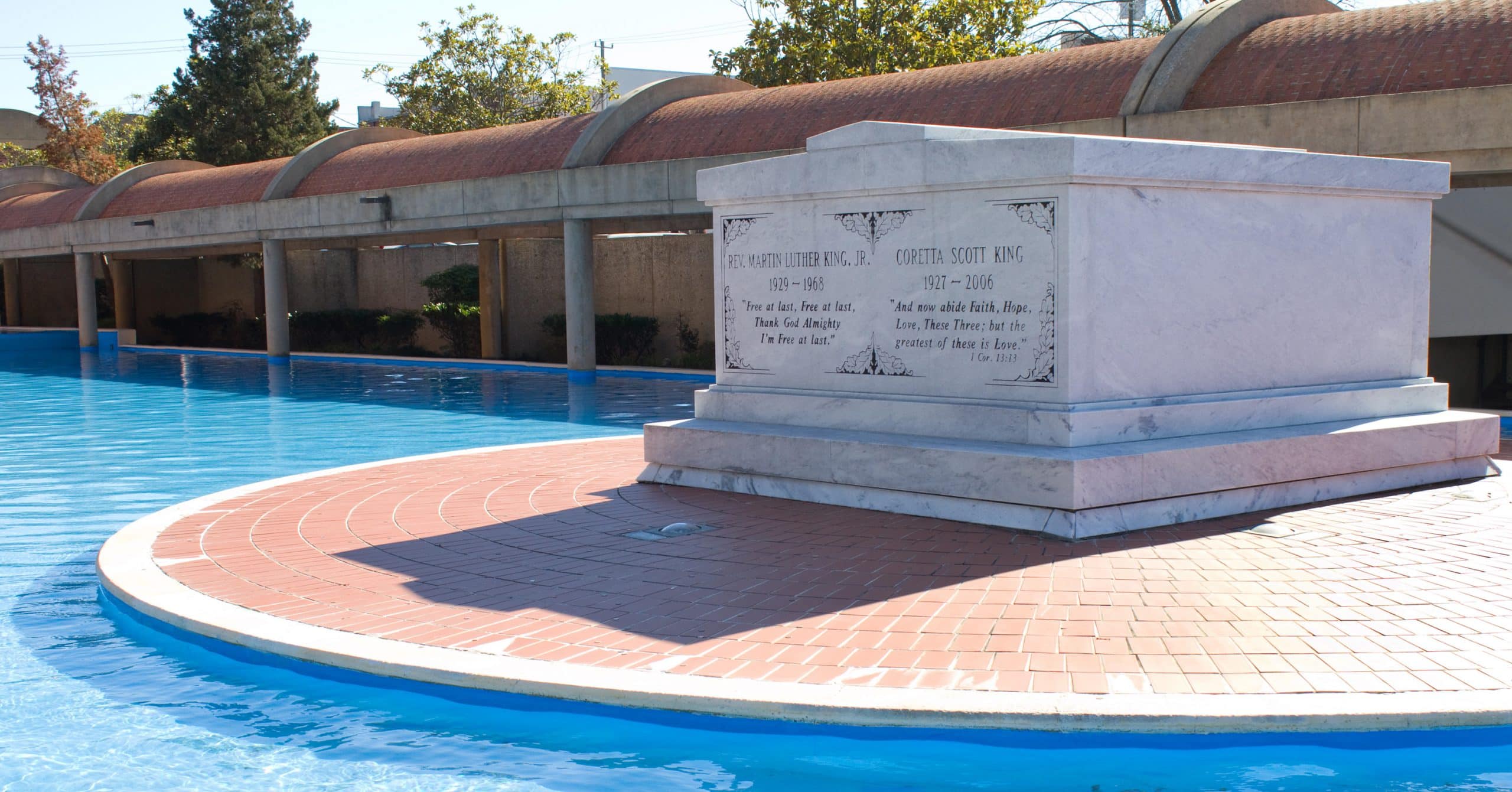 A white marble tomb for Martin Luther King Jr. and Coretta Scott King stands surrounded by a shallow blue reflecting pool, making it one of The Most Popular Student Travel Destinations for 2027, with a curved brick walkway and trees in the background.