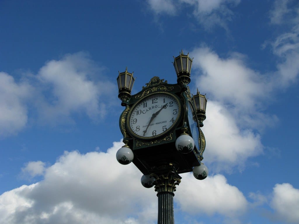A decorative, vintage-style street clock with four lanterns on top stands against a blue sky with scattered white clouds—an iconic sight among the Top 10 things to do on a Seattle Field Trip. The clock shows the time as 2:36.
