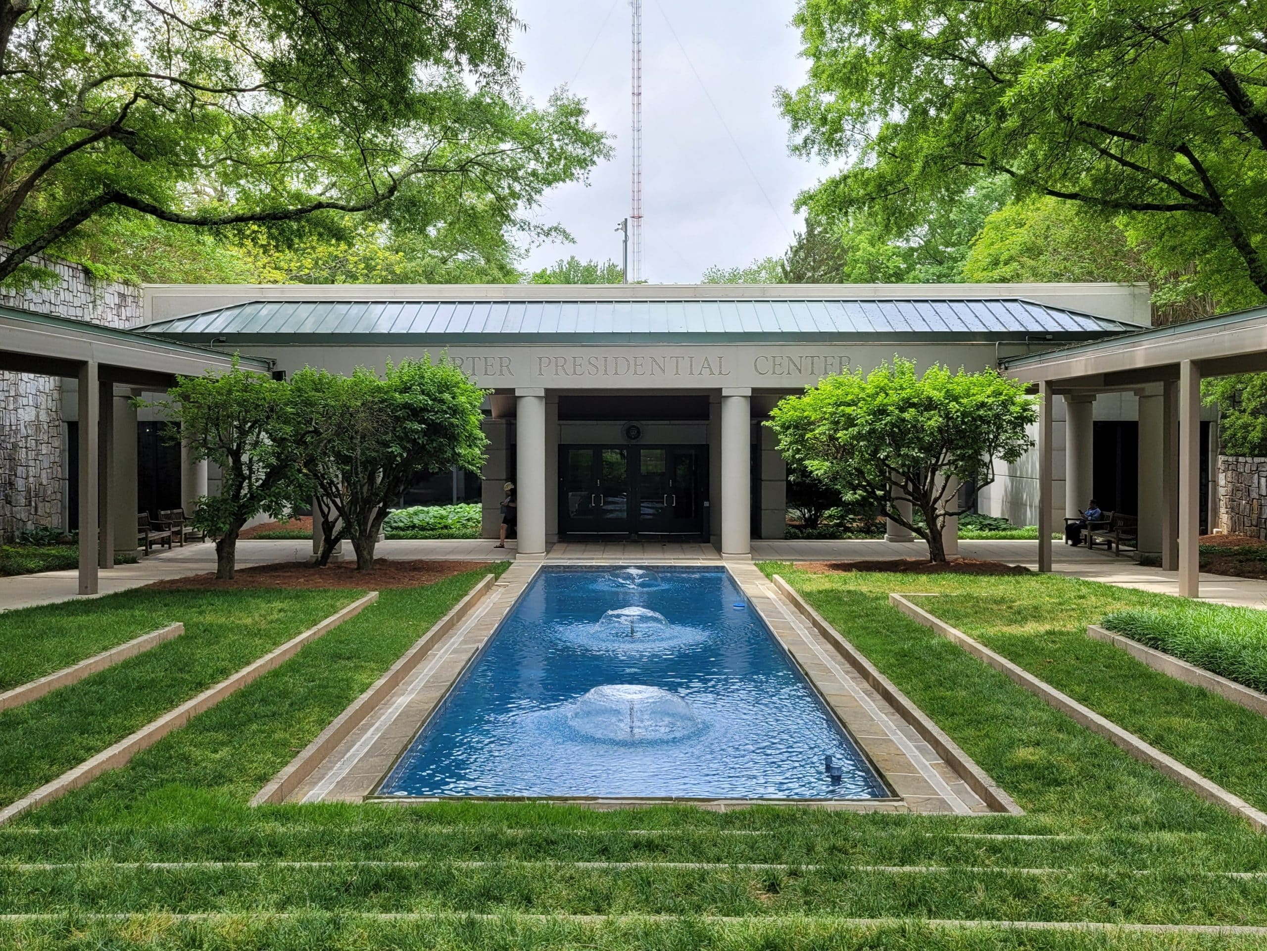 The Carter Presidential Center, a highlight of any 3 Day Atlanta Field Trip, features a reflective pool with fountains, flanked by manicured lawns and trees leading to the building's entrance.