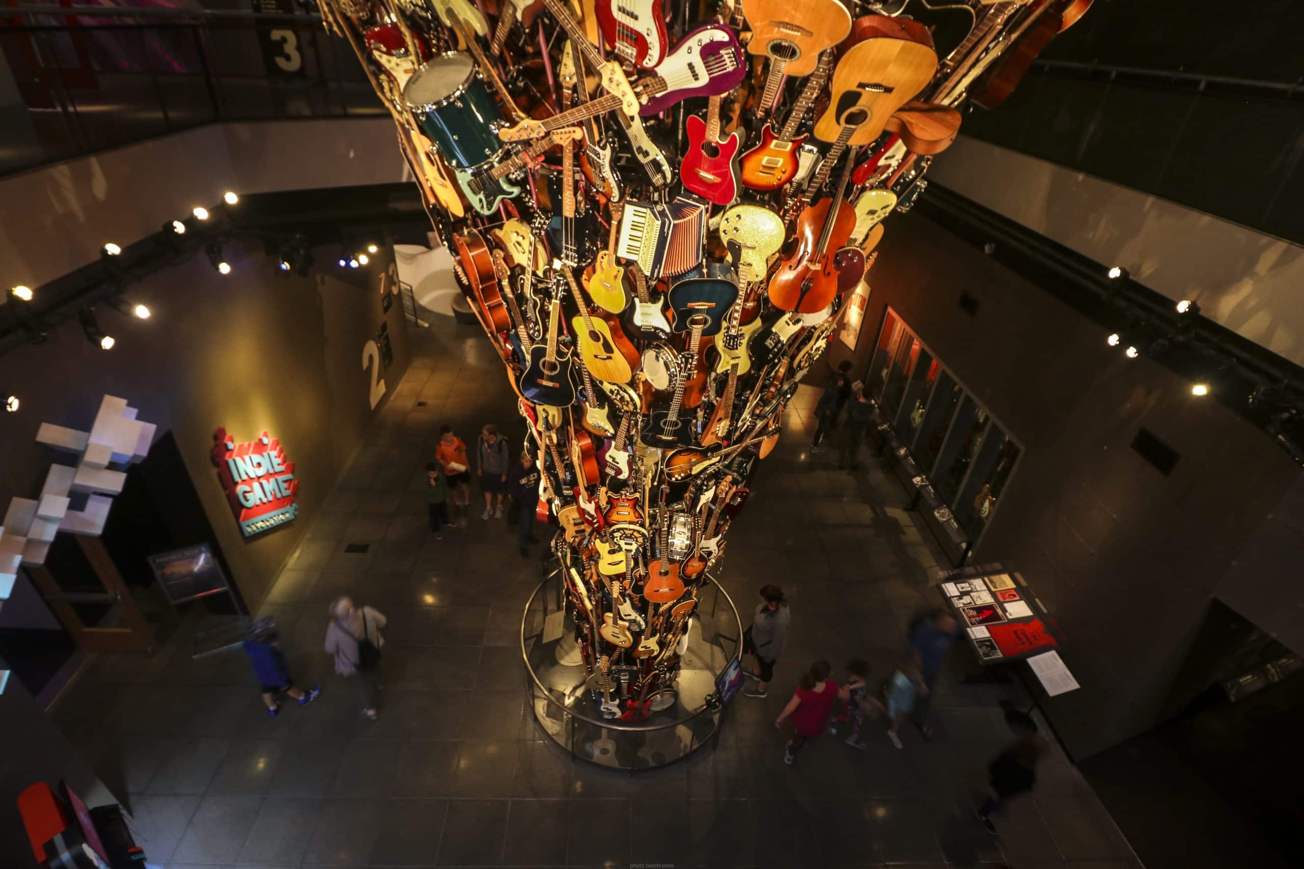 A large, dramatic sculpture made of guitars and other musical instruments forms a tornado-like spiral in a museum atrium—a must-see and among the top 10 things to do on a Seattle field trip, with visitors admiring the exhibit below.