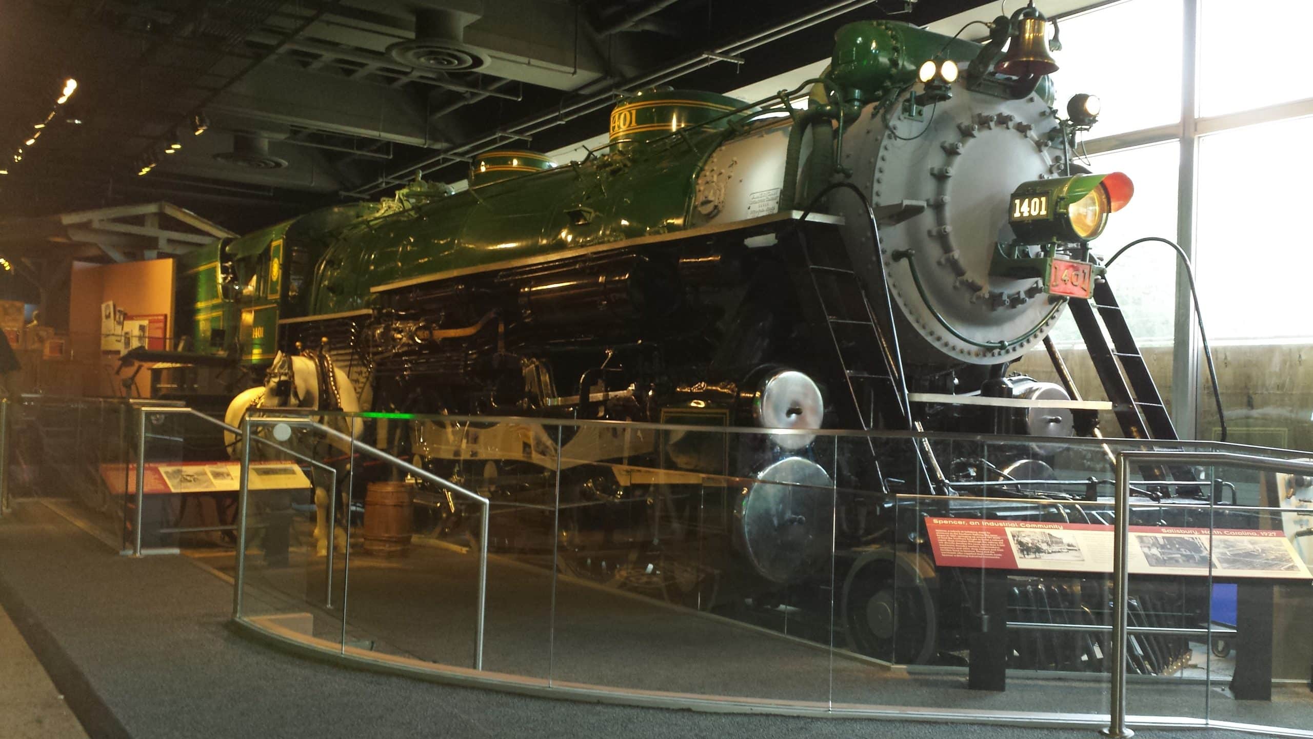 A large, green and black steam locomotive, numbered 1401, is displayed indoors behind glass barriers with informational plaques—an ideal highlight for STEM Washington DC School Trip Ideas in this well-lit museum exhibit space.