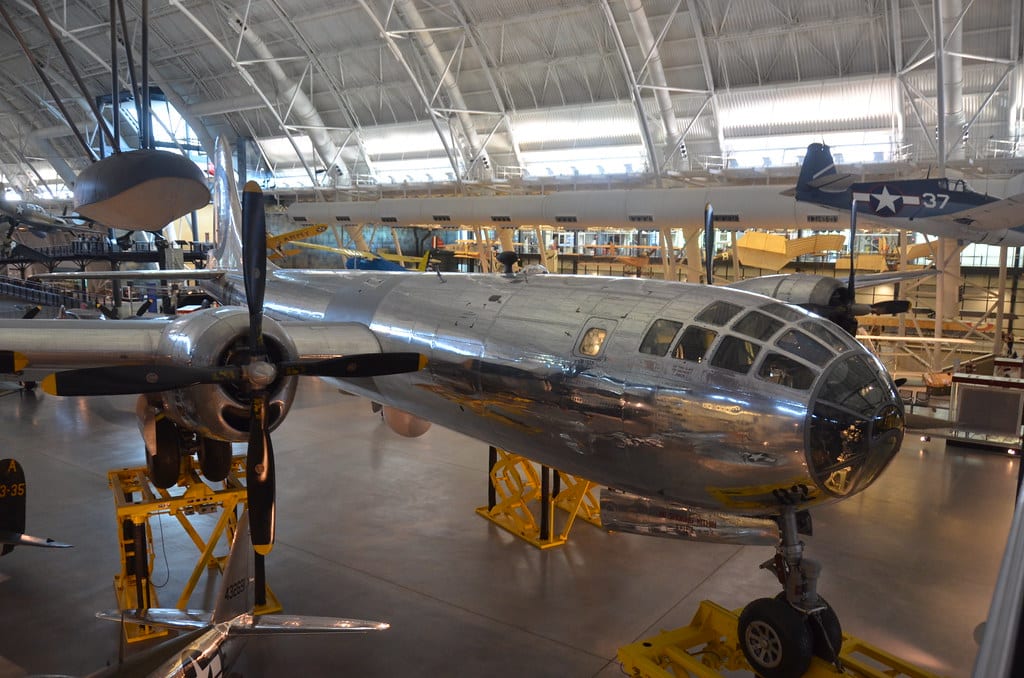 A shiny, silver B-29 Superfortress bomber is displayed in a spacious, well-lit aviation museum—one of the Best Smithsonian Museums for Student Groups—with other aircraft suspended above and visible in the background.