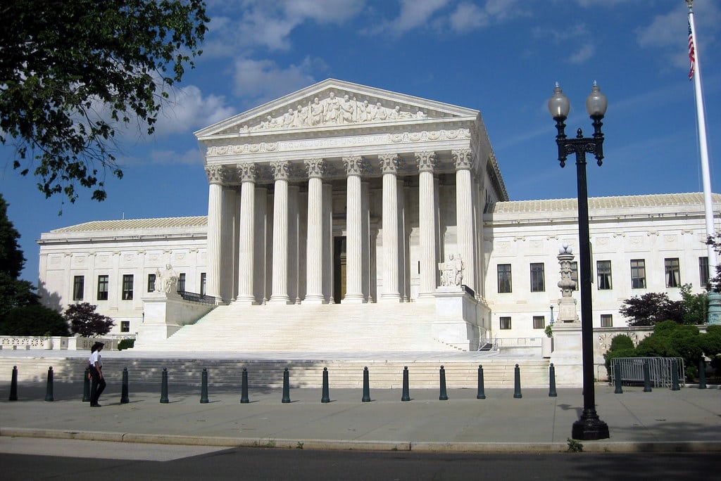 The image shows the front of the United States Supreme Court building in Washington, D.C., a landmark often visited during Educational Field Trips to Washington DC, with its large columns, wide steps, and a person walking along the sidewalk.