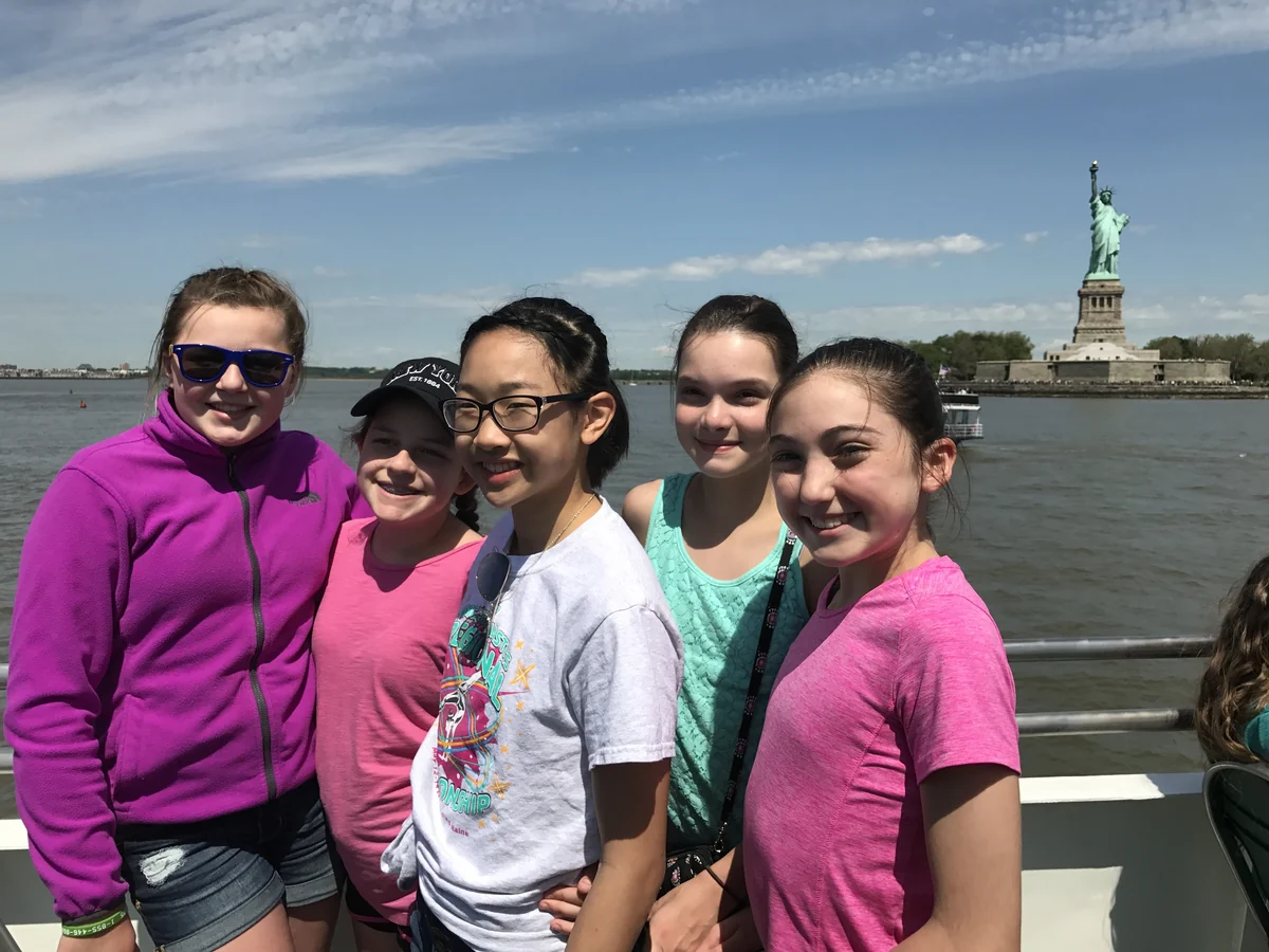 A small group of students on a boat with the Statue of Liberty behind them during a Landmark school trip to New York City