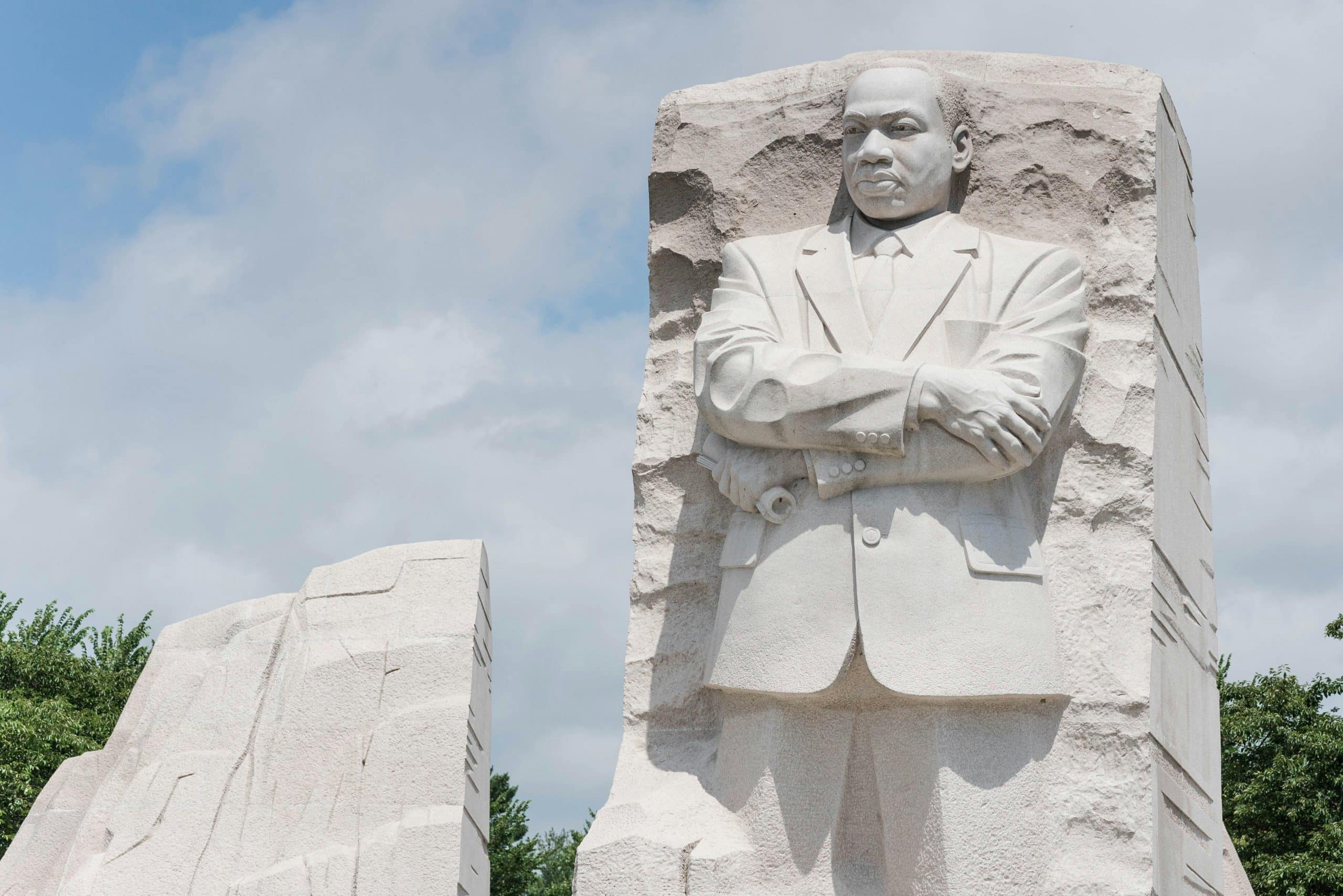 Large stone sculpture of Martin Luther King Jr. with arms crossed, emerging from a carved granite block, set outdoors against a partly cloudy sky and greenery—an inspiring stop among The Most Popular Student Travel Destinations for 2027.