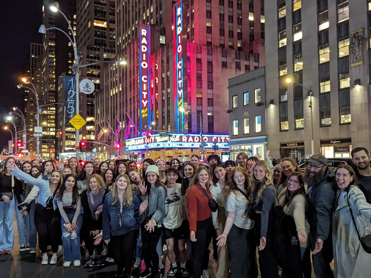 A large Landmark student group outside Radio City Music Hall in New York City in the evening