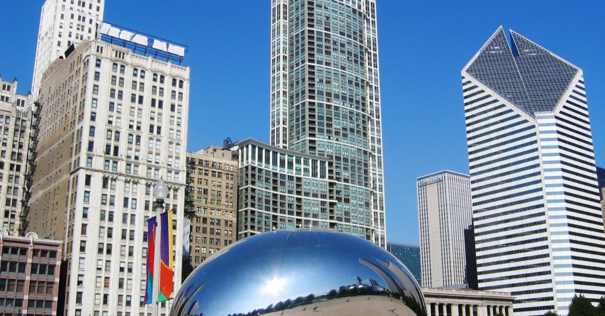 A sunny day in downtown Chicago at Millennium Park. The giant bean is in the center and there are people around.