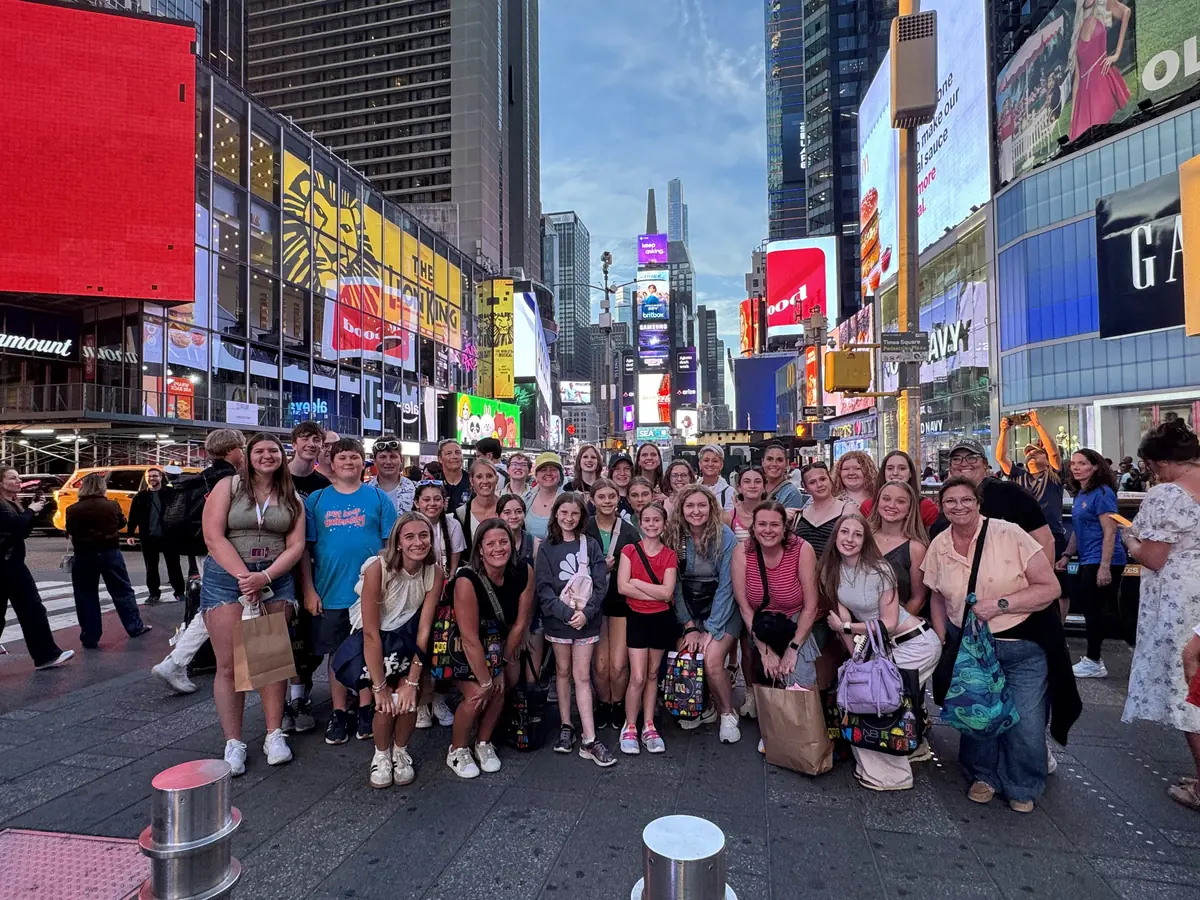 A large Landmark school group photographed in Times Square at dusk with illuminated billboards and Broadway marquees behind them