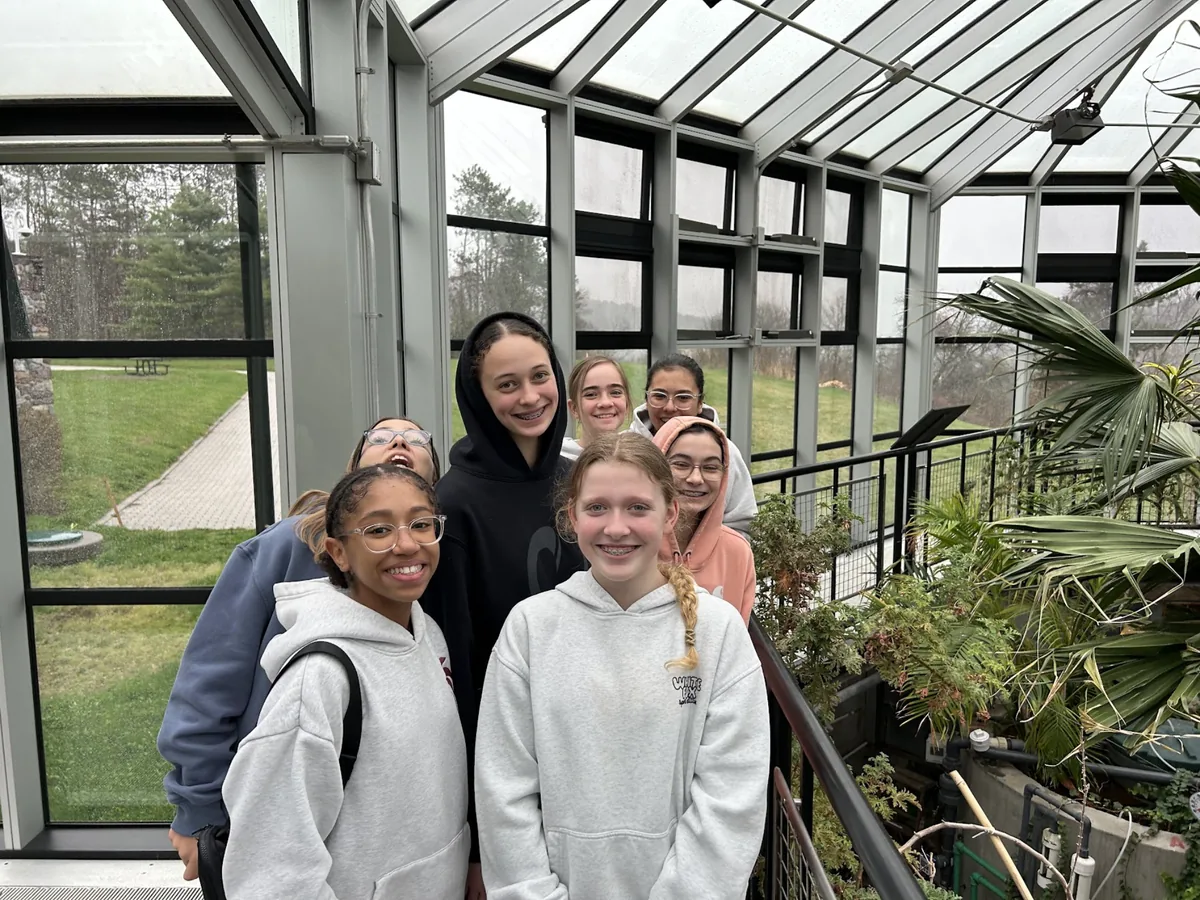 Landmark students smiling together inside a glass conservatory on a rainy day