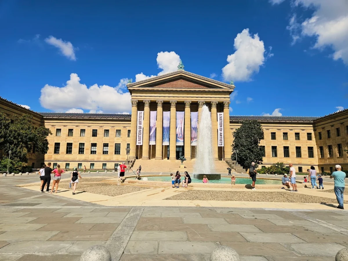 The Philadelphia Museum of Art seen across its fountain on a clear day, with banners hanging between the columns