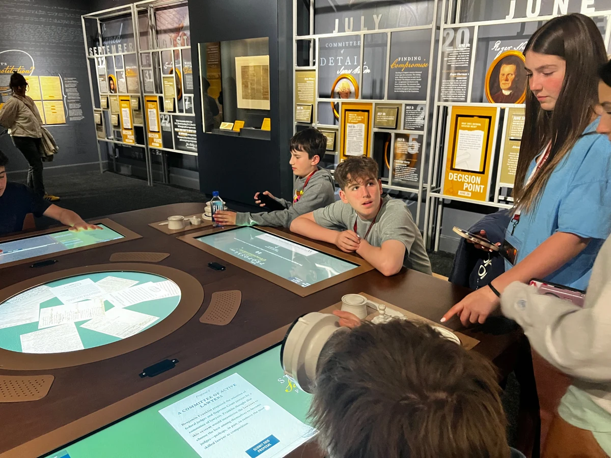 Students gathered around interactive touch tables in a Constitution exhibit, working through decision points from the drafting debates