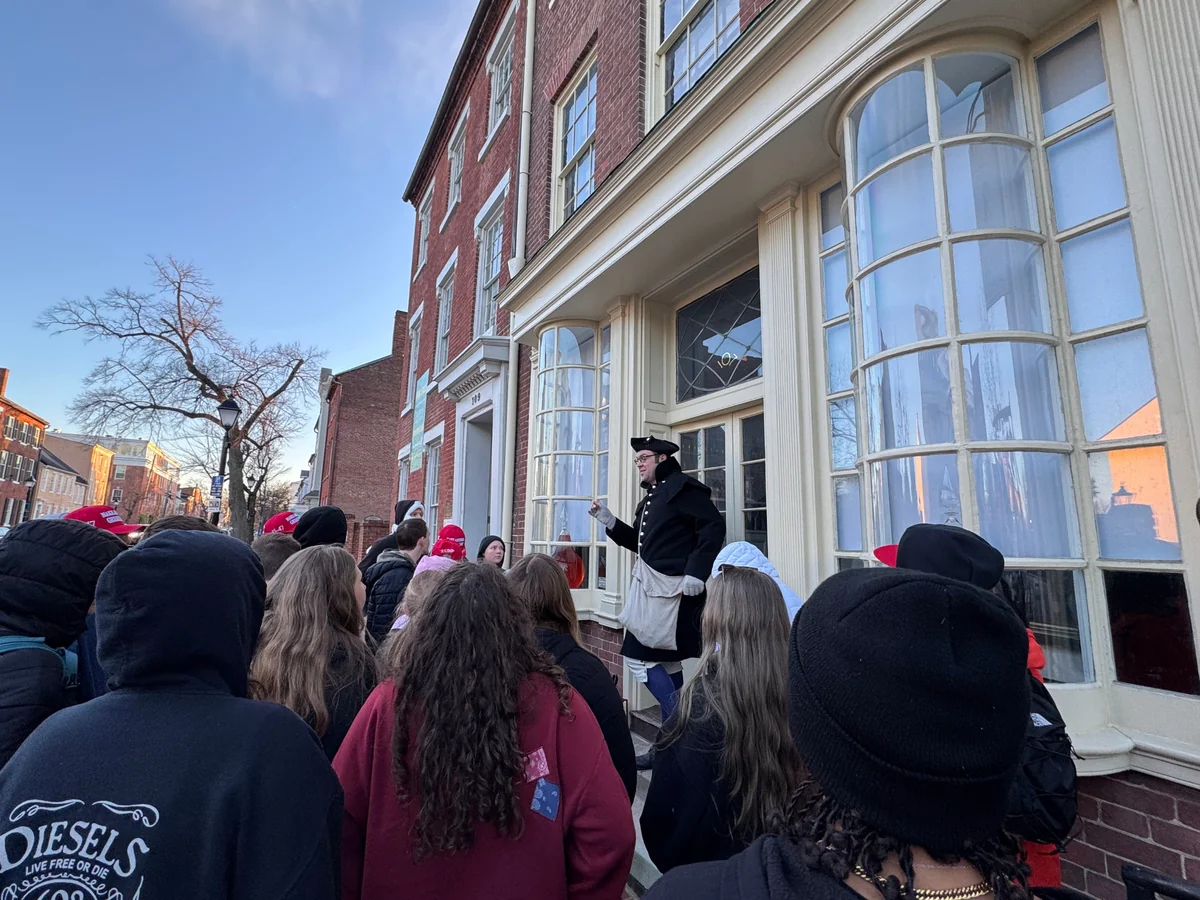 A costumed interpreter in colonial dress addressing a student group on a brick-lined Old City street in Philadelphia