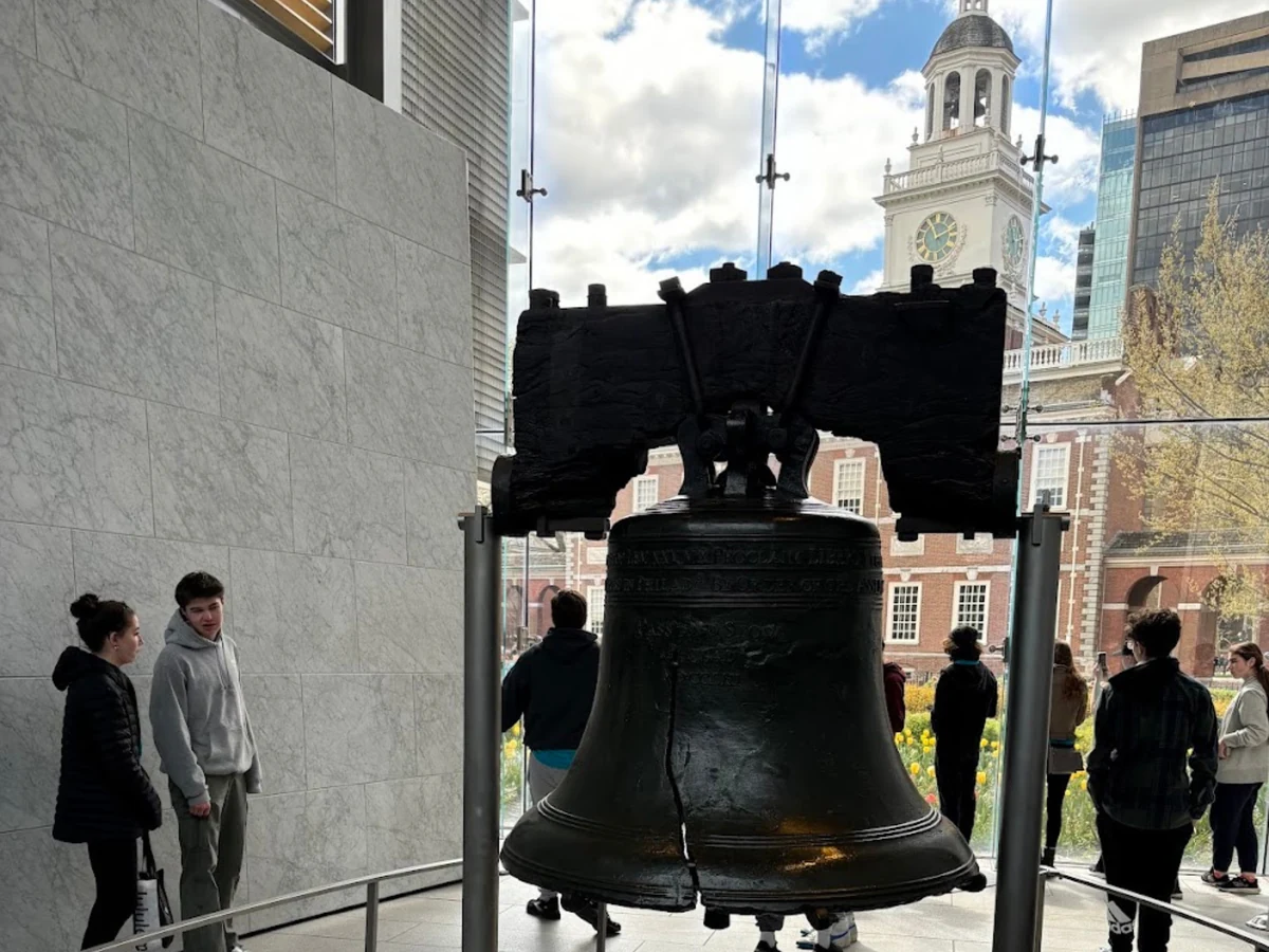 The Liberty Bell on display with Independence Hall visible through the glass wall behind it