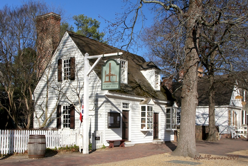 A historic white clapboard building with a brick chimney, picket fence, and sign reading "R. Charlton’s Coffeehouse & B. Ord. Office" stands under leafless trees on a sunny Colonial Williamsburg Field Trip day.