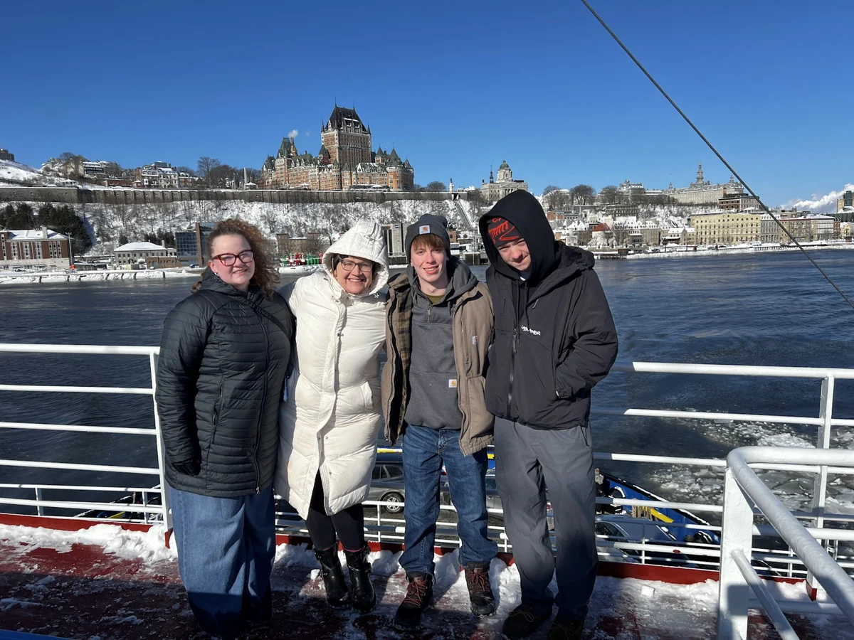 A small Landmark group of three students and a chaperone on the Quebec City ferry, with the Chateau Frontenac behind them