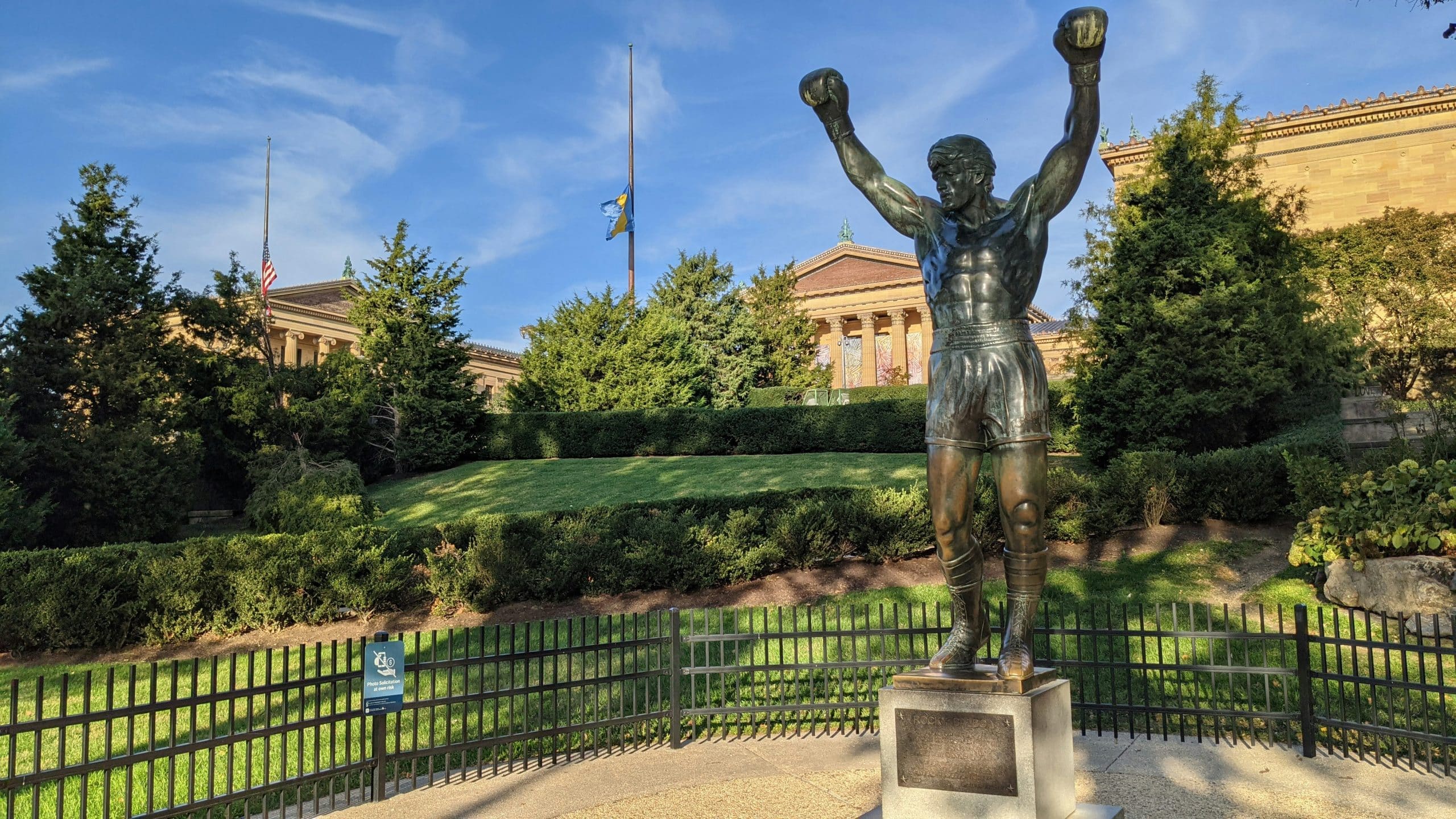A bronze statue of a boxer with raised arms stands in front of lush greenery and a classical building—an iconic spot among The Most Popular Student Travel Destinations for 2027.