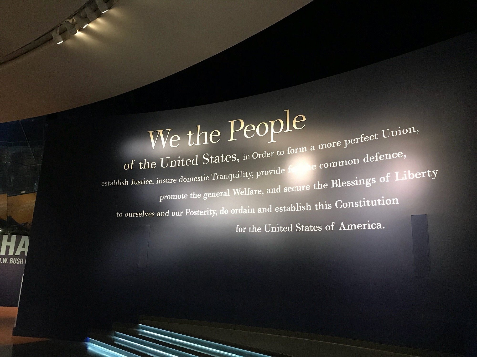 A wall at the National Constitution Center Philadelphia displays the preamble to the U.S. Constitution in large, illuminated text, beginning with "We the People" and continuing through the rest of the preamble in a museum-like setting.