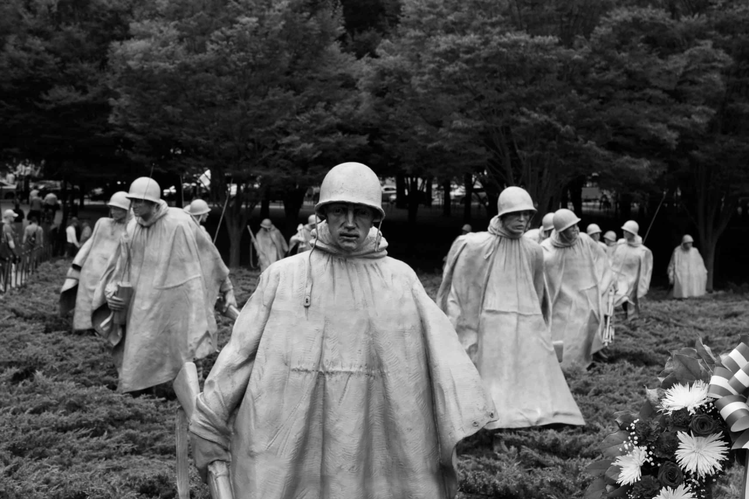Black and white photo of the Korean War Veterans Memorial, capturing life-sized soldier statues in ponchos and helmets. A powerful stop on Educational Field Trips to Washington DC, set among low bushes with trees in the background.