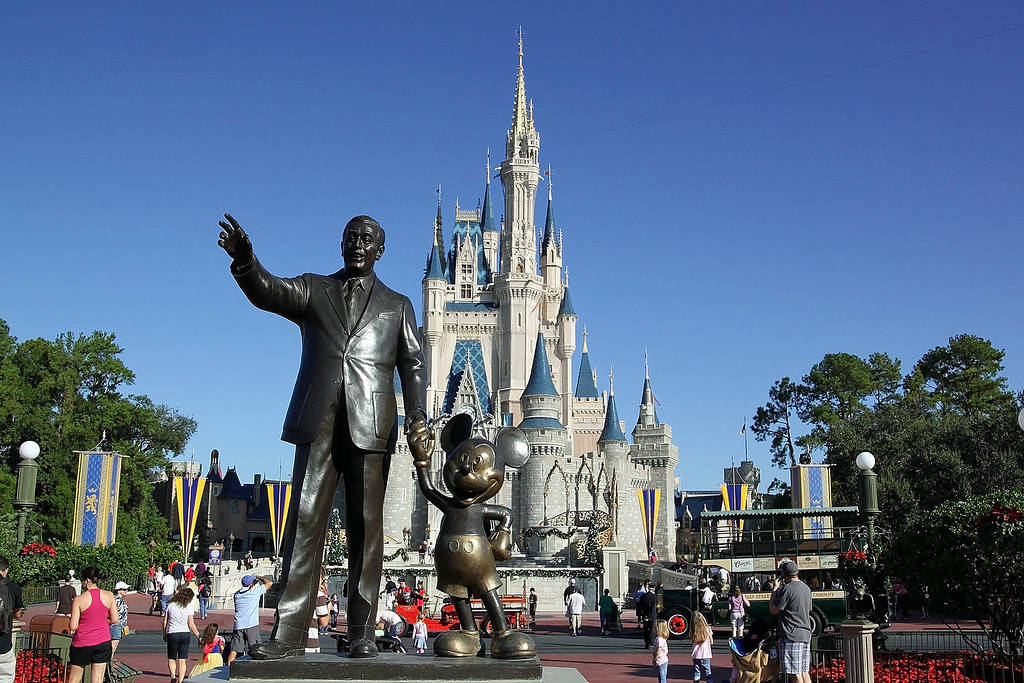 A bronze statue of a man and Mickey Mouse stands before Cinderella Castle at a busy Disney theme park, as visitors enjoy the clear blue sky—an iconic stop on any 3 Day Orlando Student Trip.