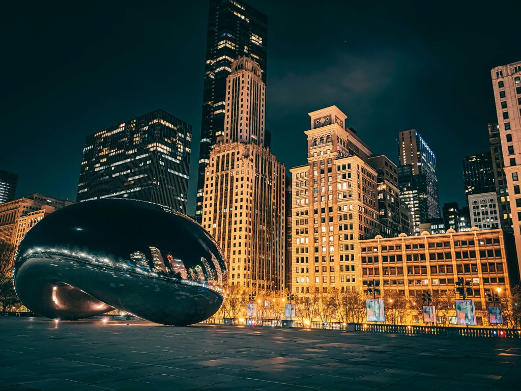 A nighttime view of Chicago’s Cloud Gate sculpture, also known as "The Bean," reflecting city lights and tall illuminated buildings—a must-see highlight on any Chicago Student Tour.