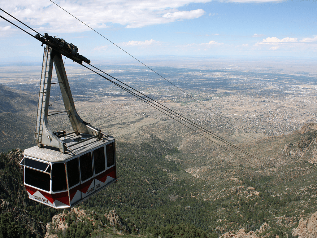 A red and white cable car travels above a forested mountain slope, offering stunning views of the city below—a perfect scene for Landmark Educational Tour Registration under a partly cloudy sky.