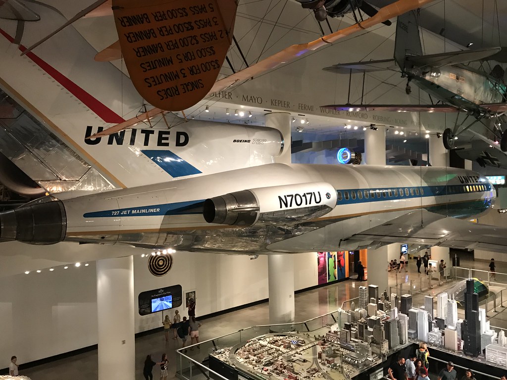A United Airlines Boeing 727 aircraft, featuring retro livery and registration N7017U, is displayed suspended in a museum. Popular for Educational Field Trips, visitors in Chicago can walk beneath it and explore a nearby city model.