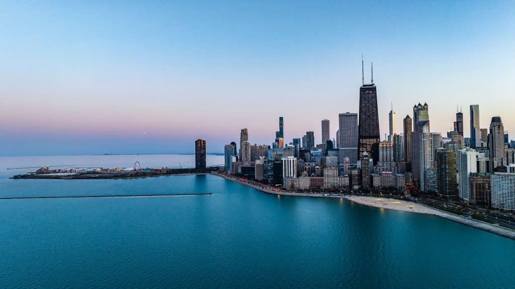 Aerial view of downtown Chicago at sunset, showing skyscrapers, Lake Michigan, and a stretch of sandy shoreline—an inspiring scene perfect for Educational Field Trips Chicago beneath a clear sky and calm blue water.