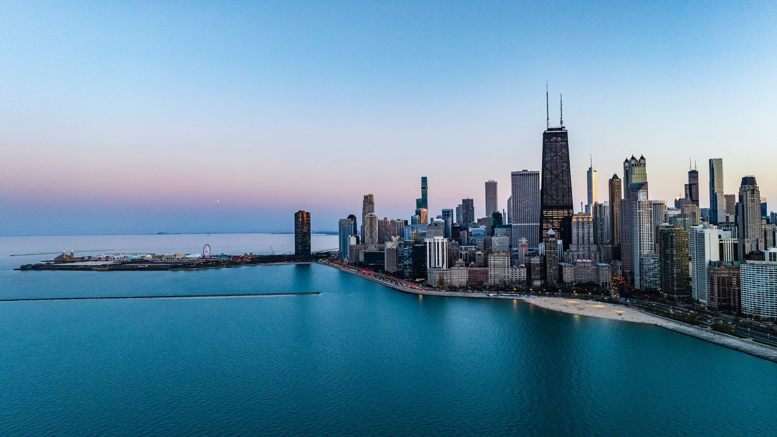 Aerial view of downtown Chicago at sunset, showing skyscrapers, Lake Michigan, and a stretch of sandy shoreline—an inspiring scene perfect for Educational Field Trips Chicago beneath a clear sky and calm blue water.