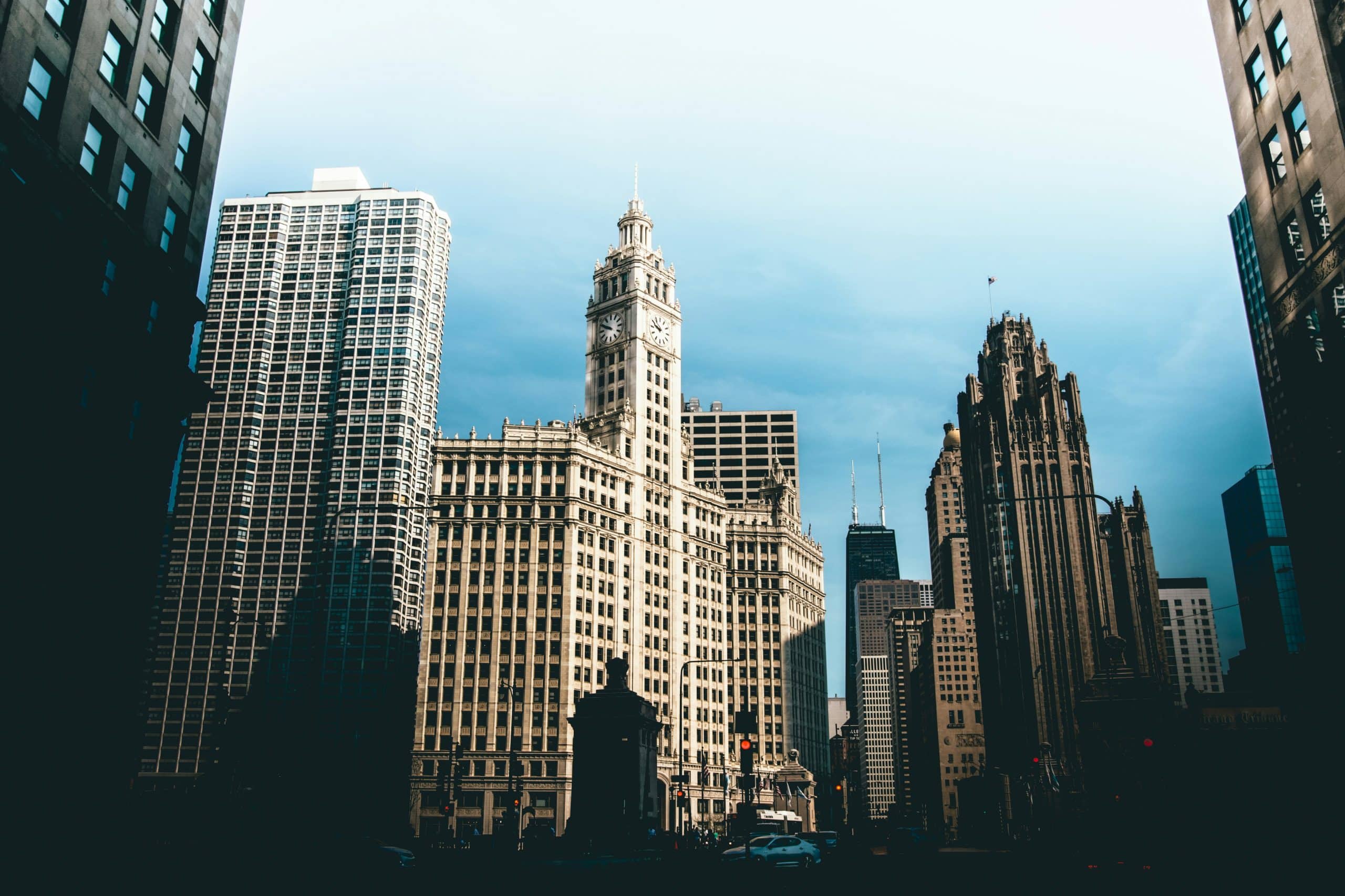 A cityscape featuring tall historic and modern buildings under a partly cloudy sky, with the sun casting dramatic shadows on the architecture—perfect inspiration for your next Chicago Field Trip.