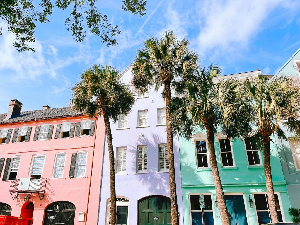 Colorful pastel buildings with large windows stand behind a row of tall palm trees under a bright blue sky—just one of the sights you'll find when exploring the top 10 things to do in Charleston SC.