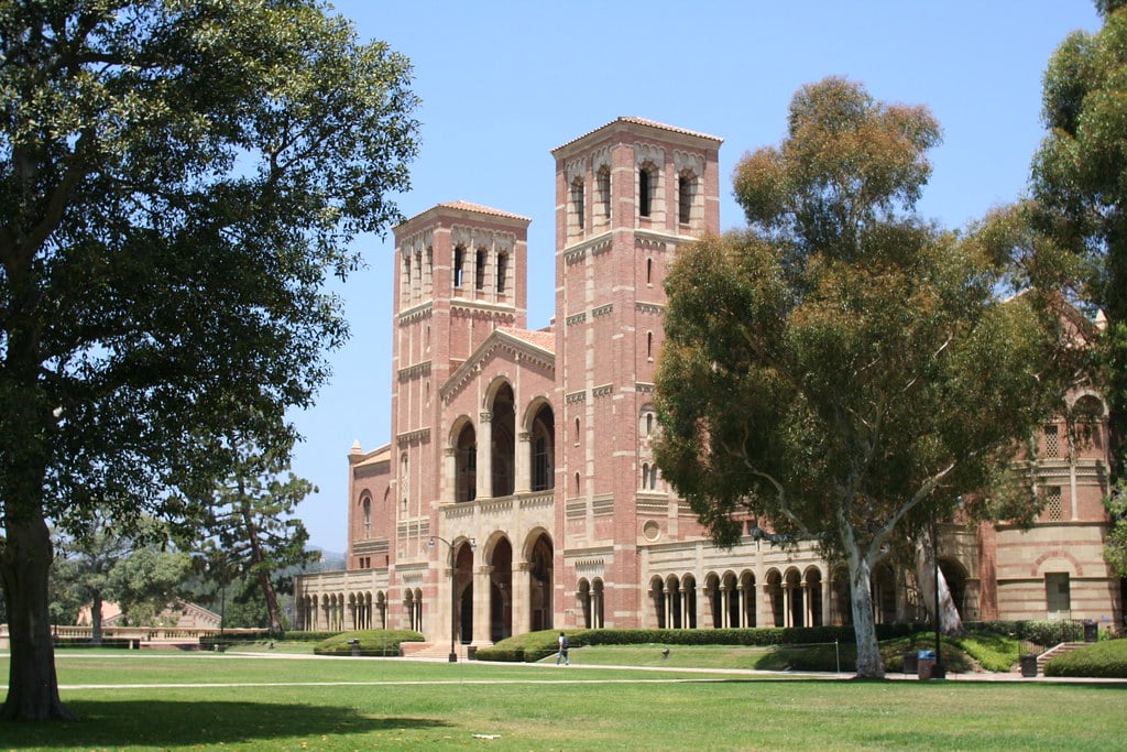 The image shows a large brick building with twin towers and arched entrances, surrounded by trees and a green lawn under a clear blue sky—an iconic sight for any Los Angeles School Trip.