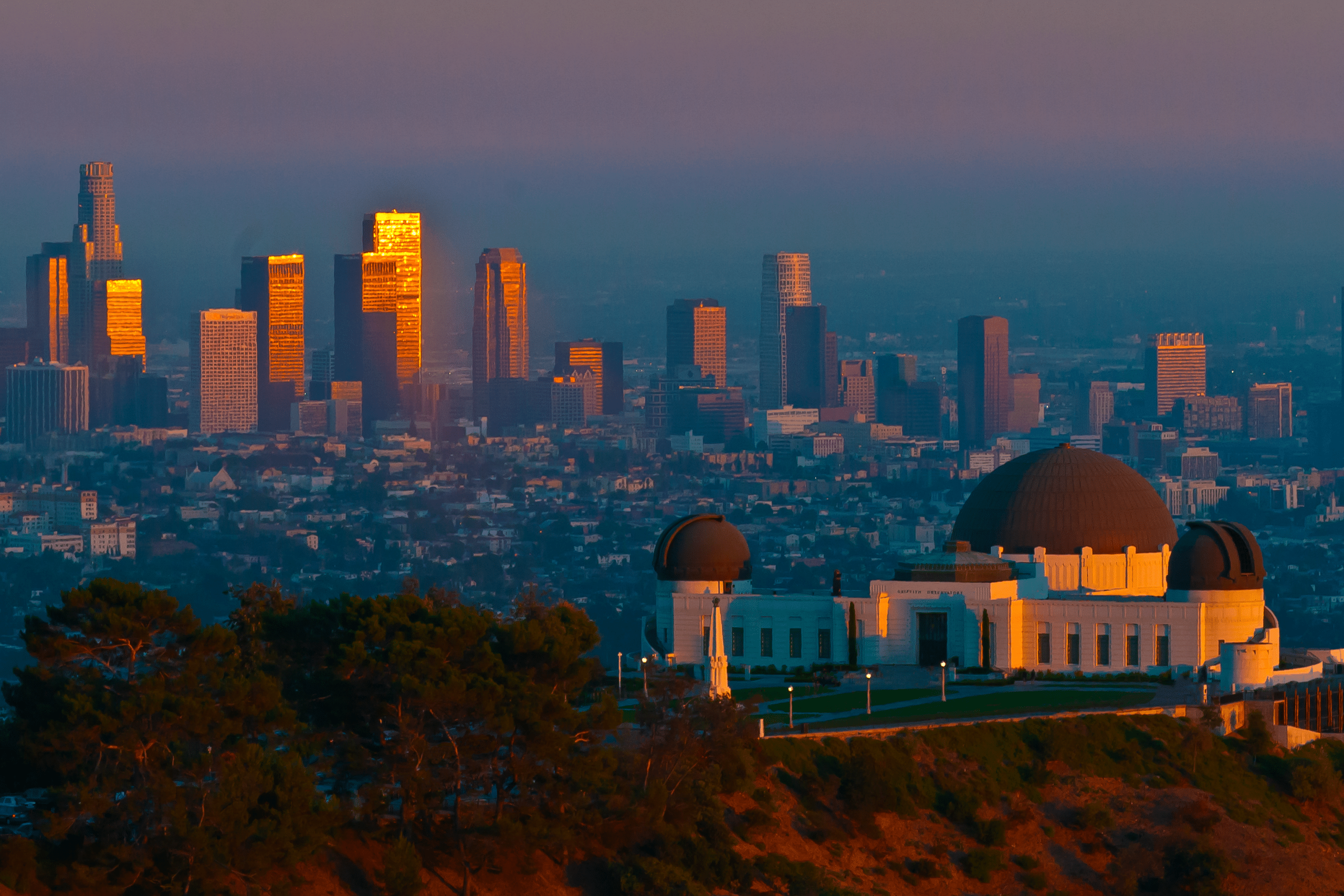The Griffith Observatory, renowned for hosting some of the Best Educational Tours in California, sits on a hilltop at sunset as the Los Angeles skyline reflects the warm orange glow of the setting sun.