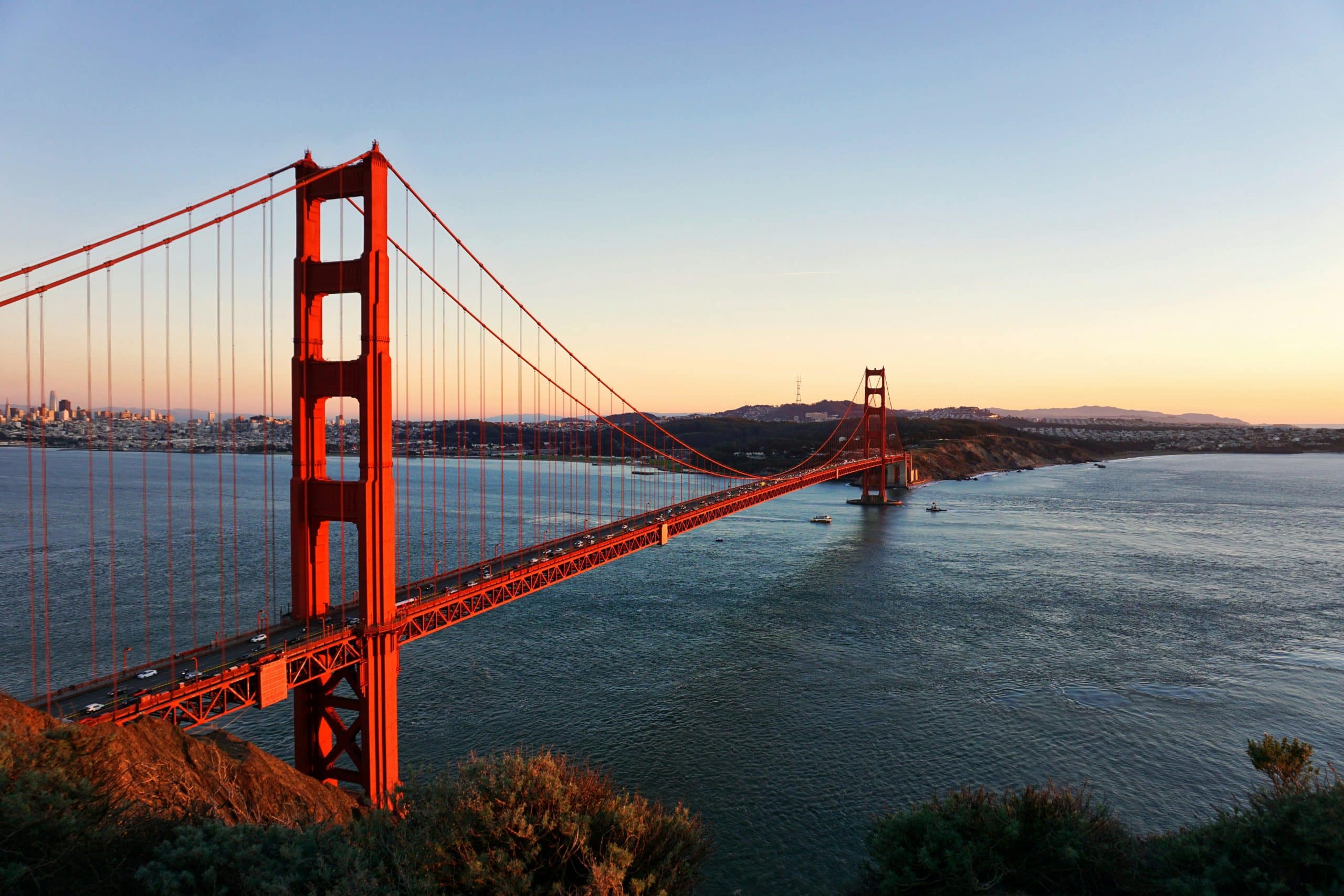 The Golden Gate Bridge stretches across the water at sunset, its iconic red towers and suspension cables glowing—an unforgettable sight often featured on the Best Educational Tours in California connecting San Francisco to Marin County under a clear sky.