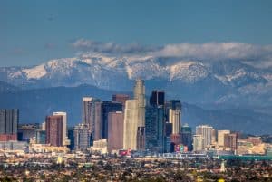Downtown Los Angeles skyline with tall modern buildings in the foreground and snow-capped mountains in the background under a clear blue sky—an inspiring view for those on the Best Educational Tours in California.