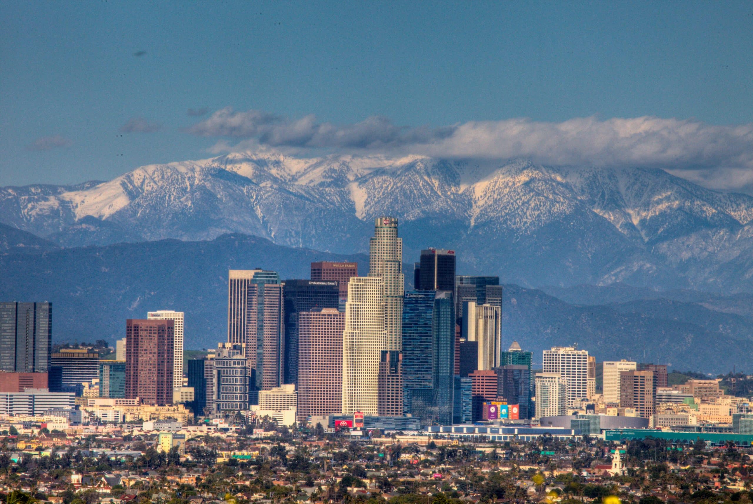 Downtown Los Angeles skyline with tall modern buildings in the foreground and snow-capped mountains in the background under a clear blue sky—an inspiring view for those on the Best Educational Tours in California.