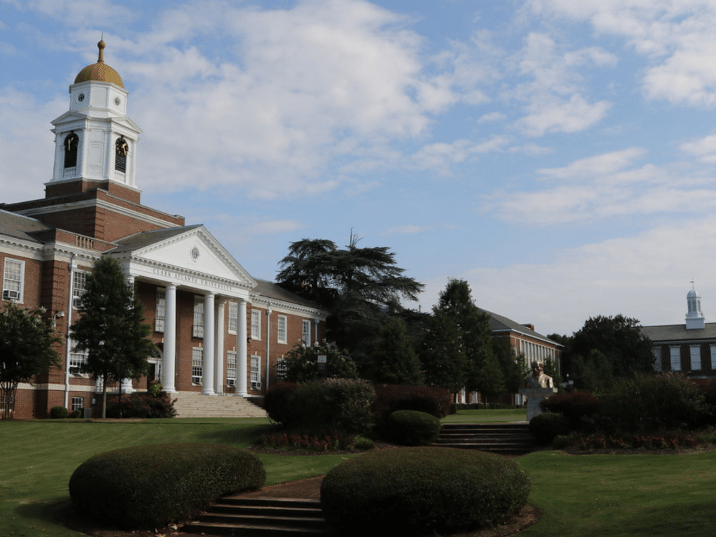 A brick building with white columns and a gold-domed clock tower sits on a manicured campus lawn, offering an inviting setting for Landmark Educational Tours Registration beneath a partly cloudy sky.