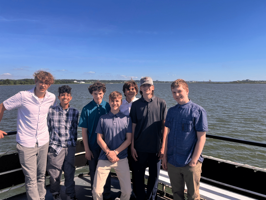 Seven teenage boys stand together on a boat under a clear blue sky, smiling at the camera on a sunny day during their Landmark Educational Tours Registration adventure.