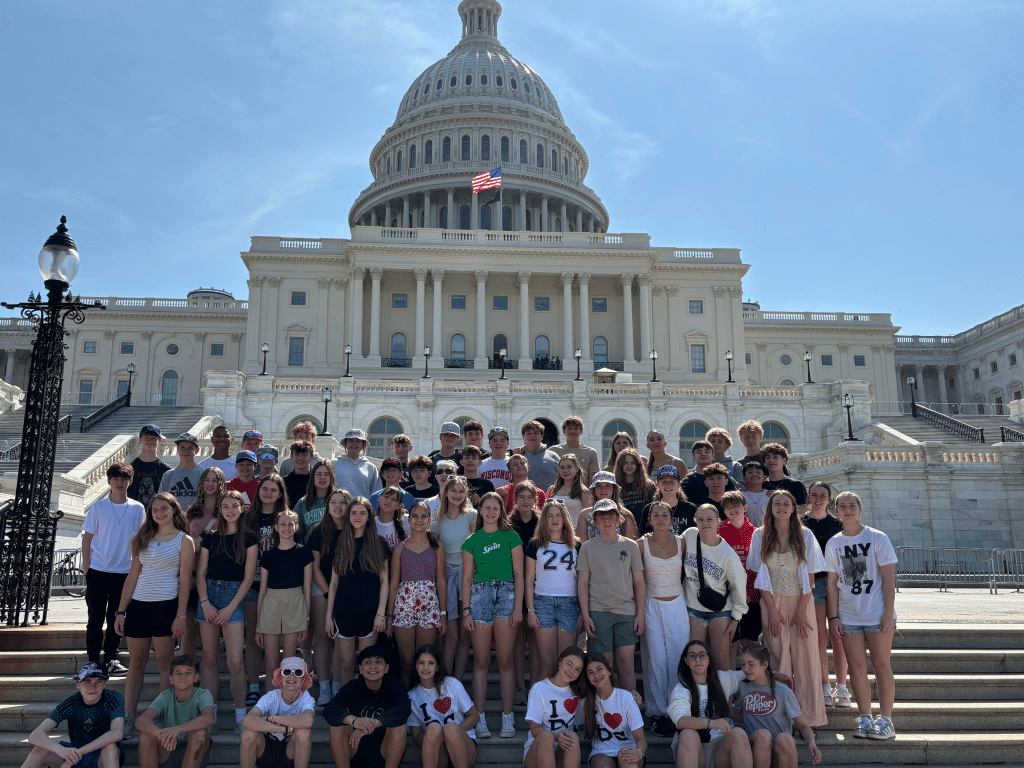 A large group of teens poses for a photo on the steps in front of the U.S. Capitol building, enjoying a bright, sunny day during their Landmark Educational Tours Registration, with the American flag visible above the dome.
