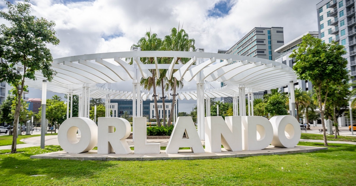 White block letters spell out "Orlando" in a park. It's sunny outside and the grass is green and healthy.