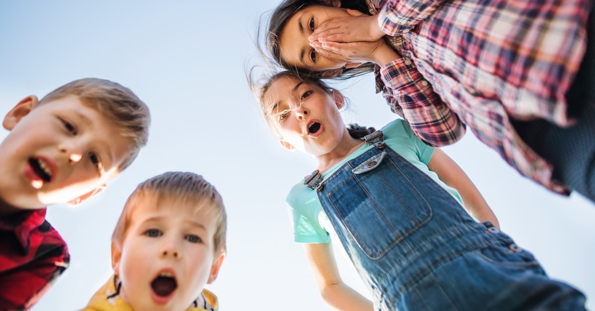 A group of four young students stand outside and stare in shock at the camera. They're looking downward.