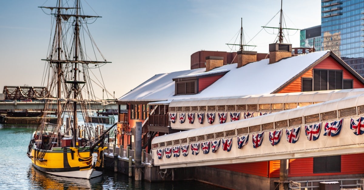A nighttime view of the Boston Harbor with a boat docked at the marina and American flag drapes hanging from the banister.