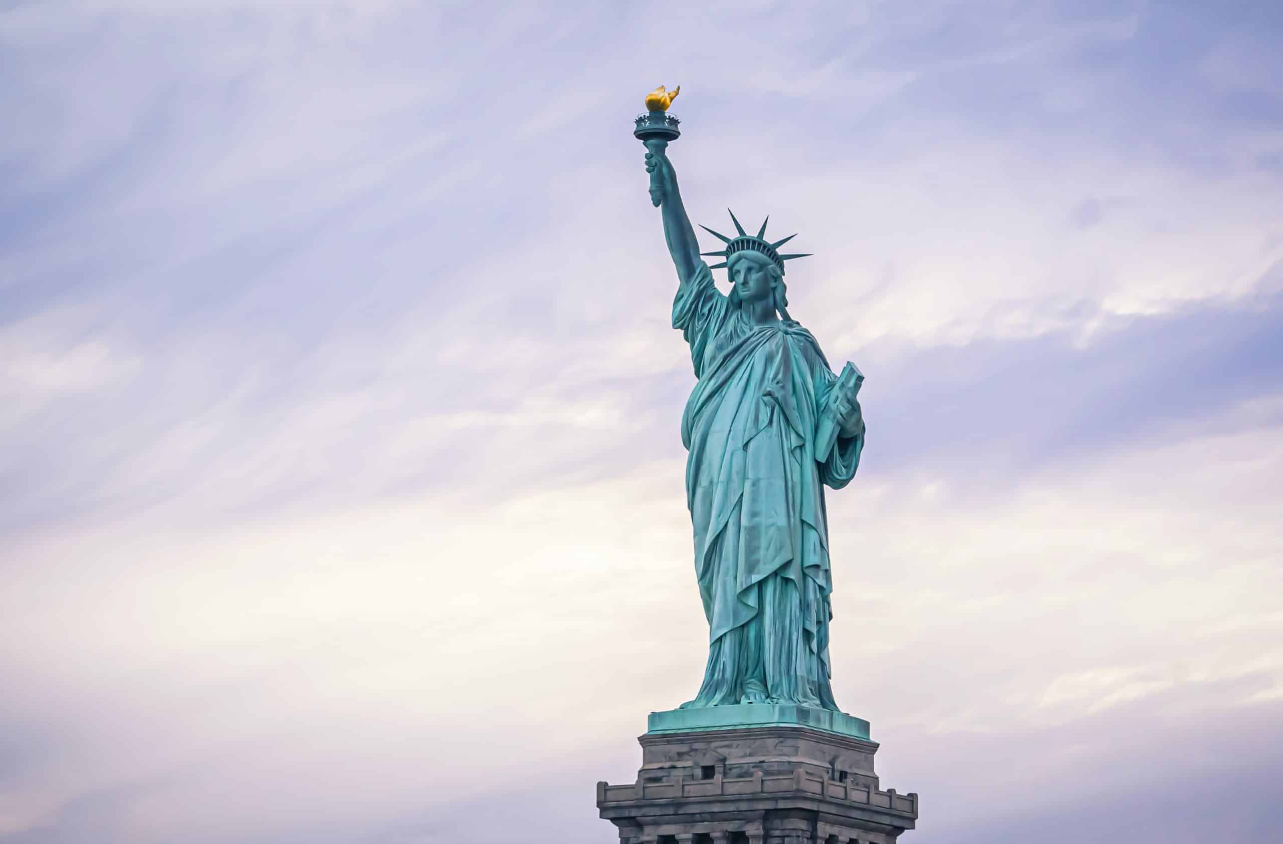 The Statue of Liberty stands tall against a cloudy sky, holding a torch in her right hand and a tablet in her left—an inspiring sight for Field Trips NYC, symbolizing freedom and hope.