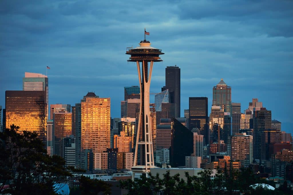 The Space Needle stands in the center of Seattle’s skyline at sunset, highlighted by golden sunlight—an iconic sight for any Seattle School Trip, with surrounding skyscrapers aglow and a cloudy blue sky overhead.