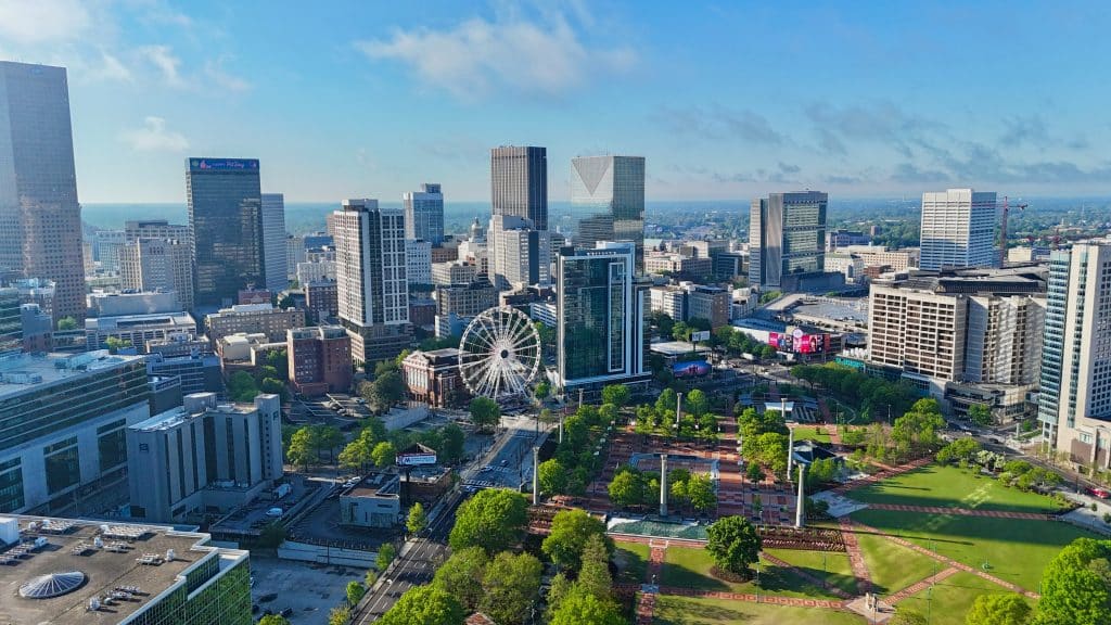 Aerial view of downtown Atlanta, Georgia, featuring skyscrapers, a large Ferris wheel, and Centennial Olympic Park—an exciting destination for an Atlanta and Alabama HBCU Field Trip under a bright blue sky.
