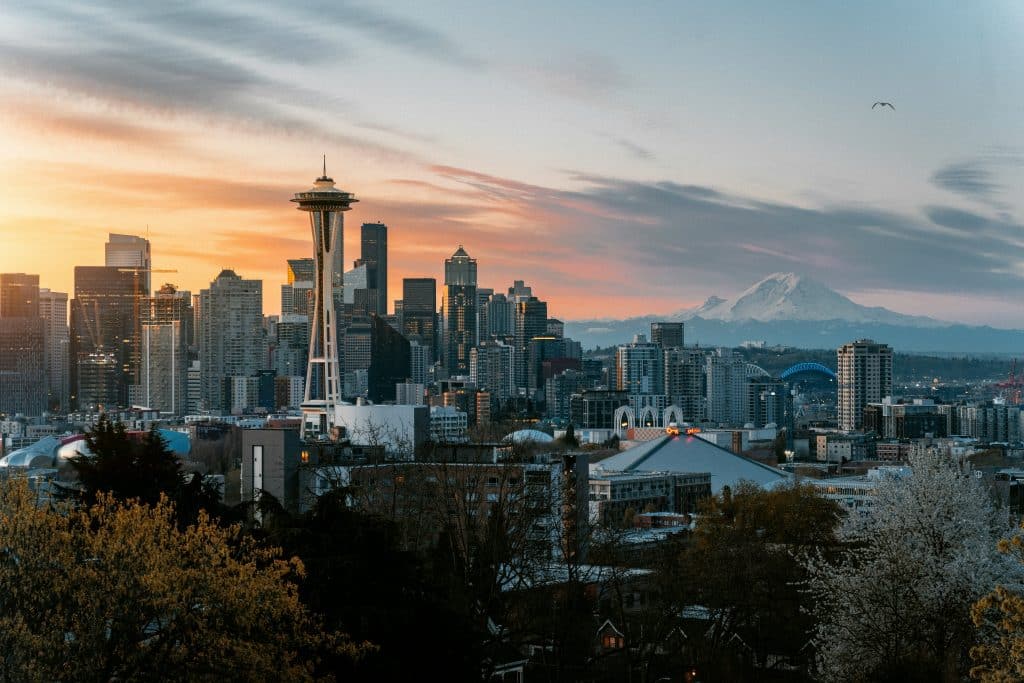 Seattle city skyline at sunset featuring the Space Needle, downtown skyscrapers, and Mount Rainier in the background—an iconic scene you won't want to miss on your Top 10 things to do on a Seattle Field Trip list. Colorful clouds and trees complete the view.