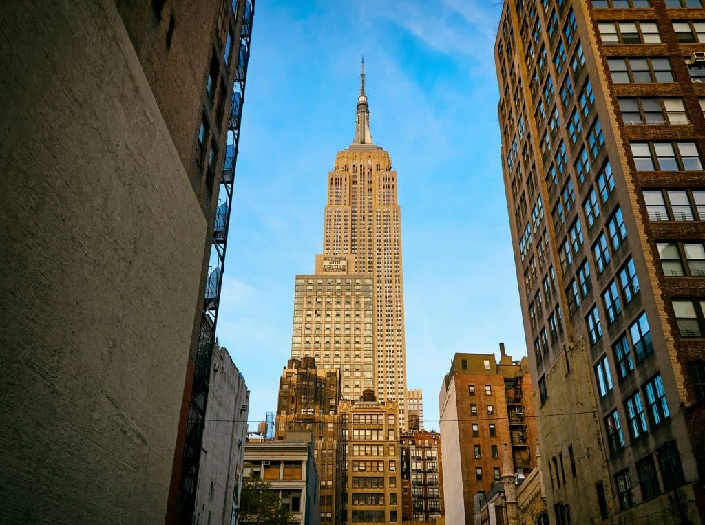 The Empire State Building stands tall between surrounding city buildings, with a clear blue sky in the background—making it one of the top NYC field trip ideas for students and visitors alike.
